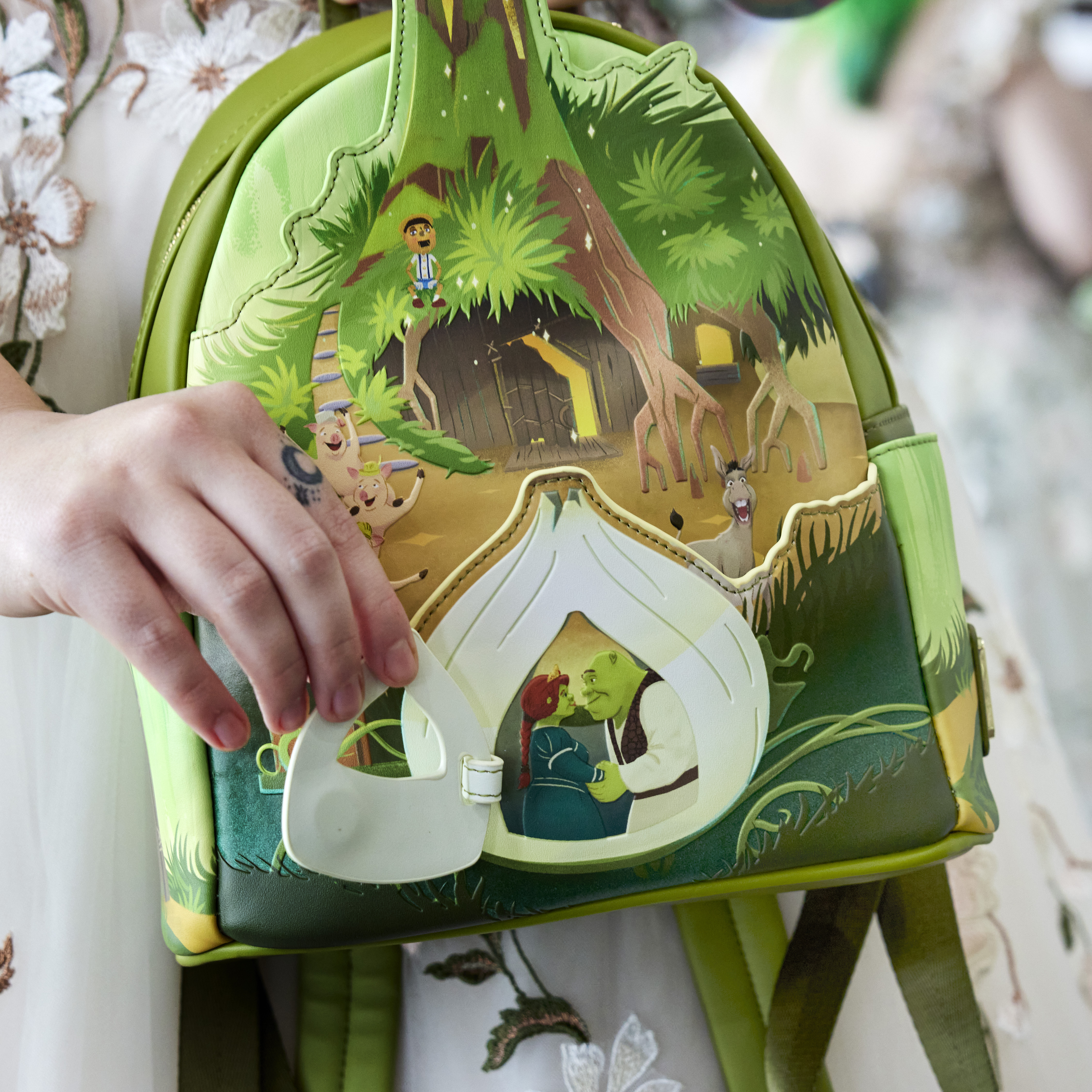 Woman holding the Shrek bag and holding open the onion carriage door to reveal Fiona and Shrek behind it.